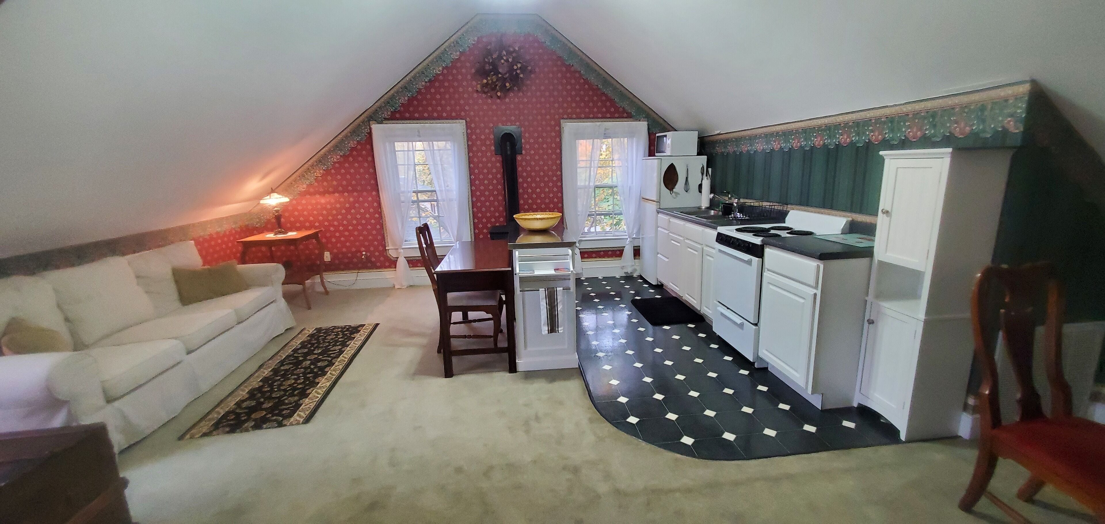 Um quarto pequeno e acolhedor com um sofá branco, uma mesa de jantar e uma cozinha compacta.