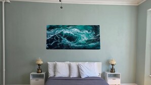 Un dormitorio con cama, dos mesitas de noche con lámparas, un ventilador de techo y un cuadro abstracto grande en la pared.