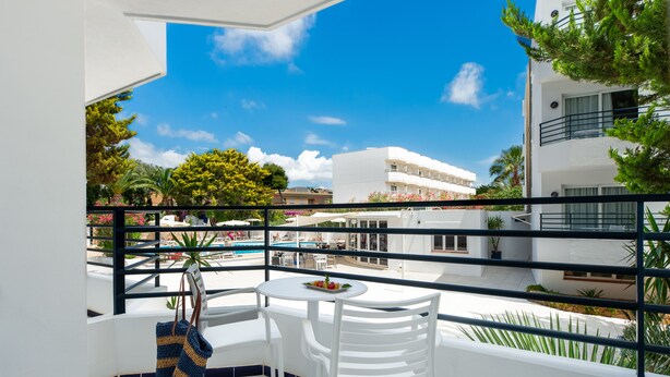 Un balcón con sillas y mesa blancos, con vistas a una piscina y edificios.