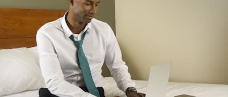 A man sitting on a bed with a laptop, wearing a white shirt and a patterned tie.