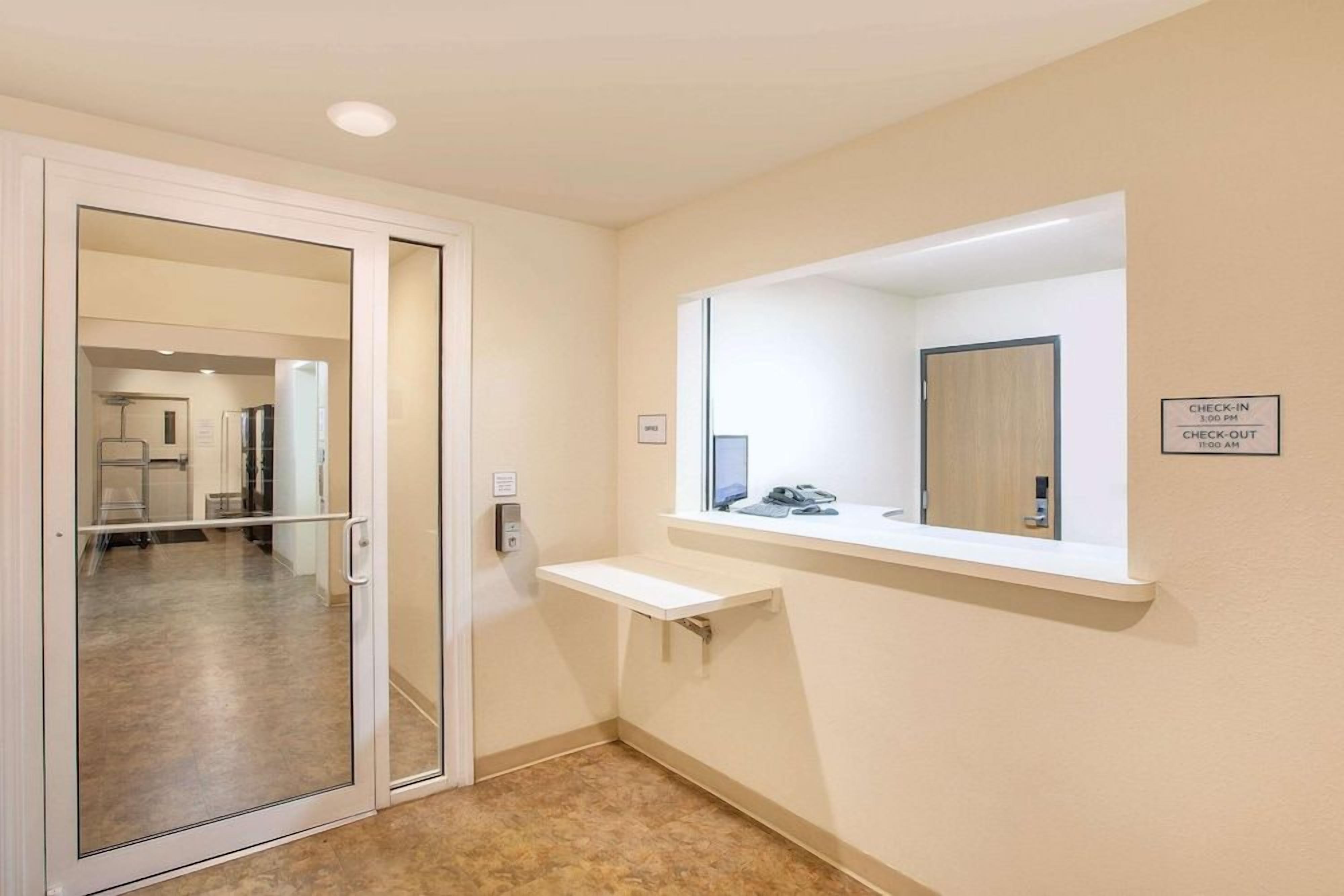 A hotel room with a sliding glass door, a small window with a mirror, and a check-in/check-out sign on the wall.