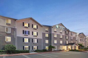 A multi-story hotel with a modern design, featuring a prominent logo on the facade. - WoodSpring Suites Jacksonville Beach Blvd (Jacksonville)