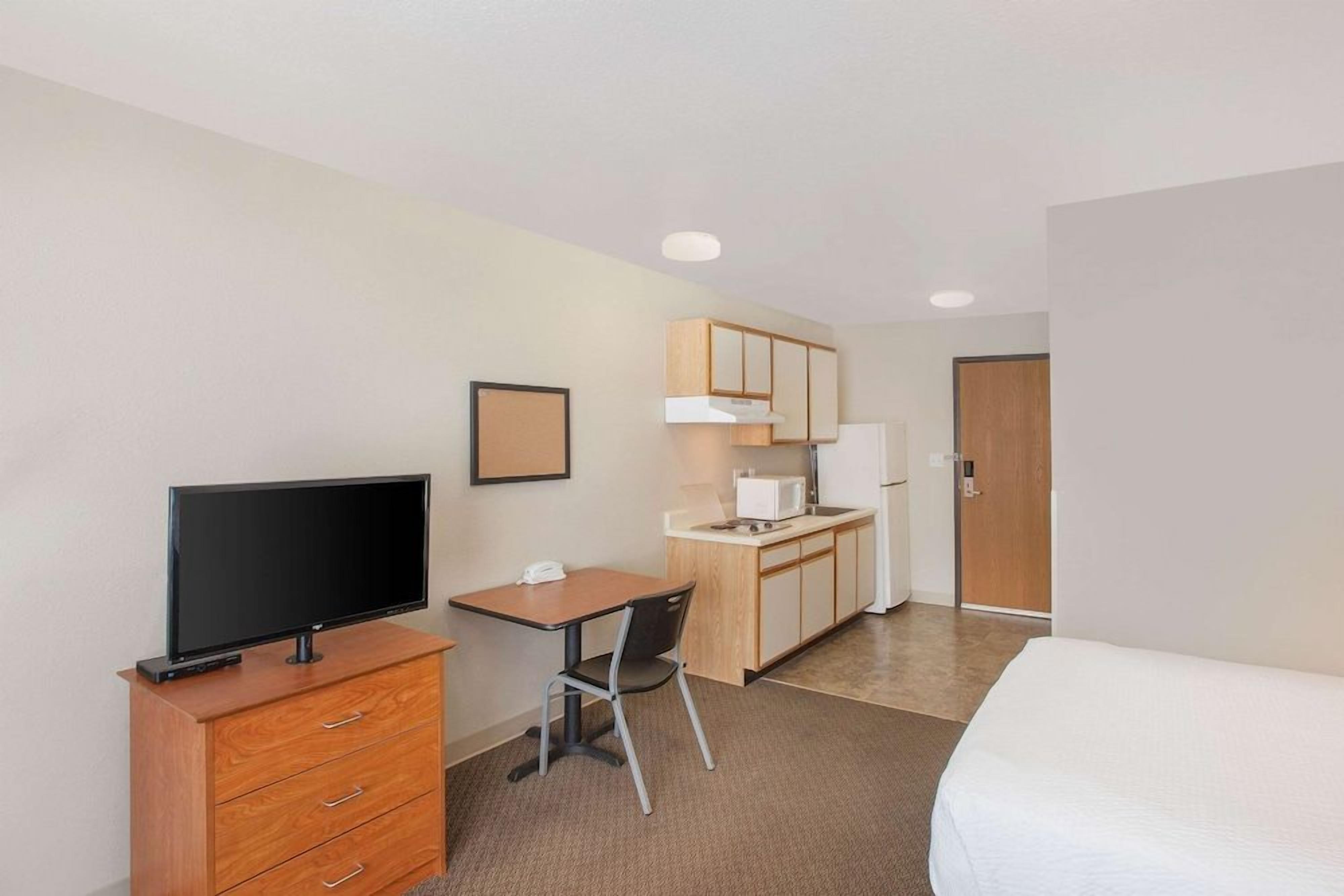A hotel room with a bed, a TV, a desk with a chair, a microwave, and a cabinet.