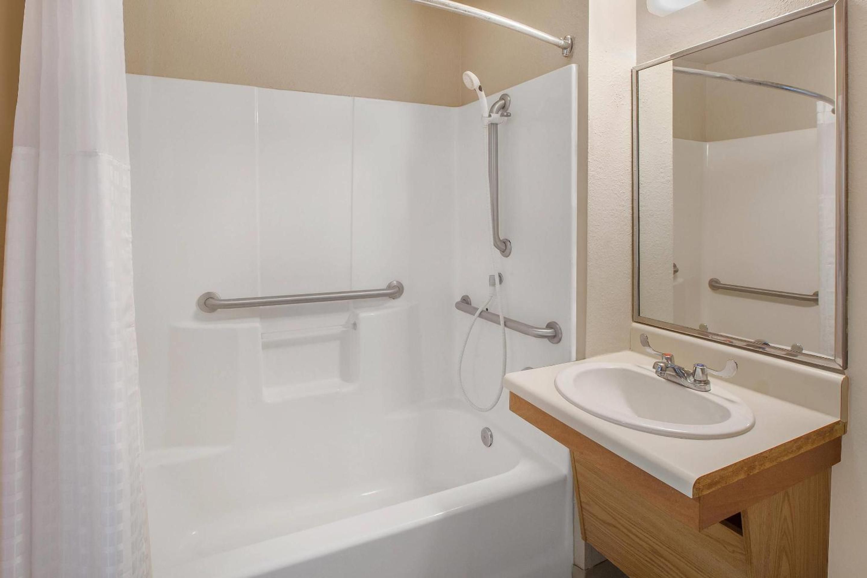 A bathroom with a white bathtub, a sink with a mirror, and a shower area with grab bars.