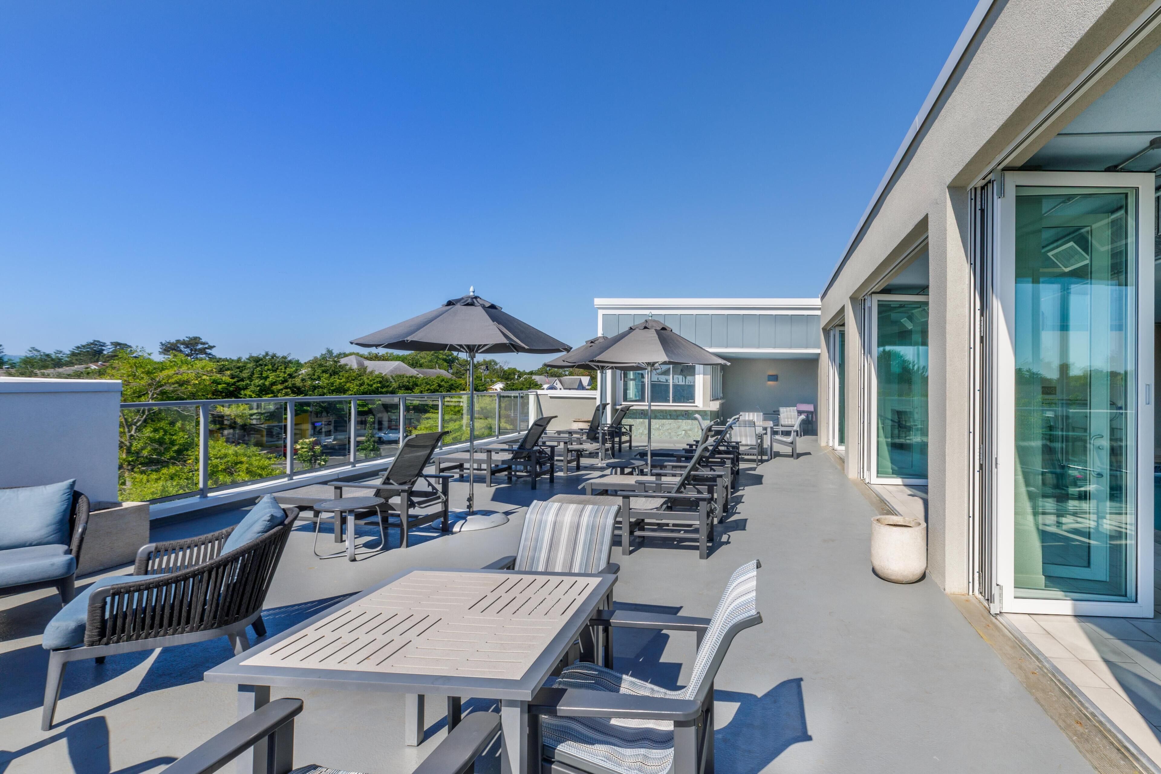 A rooftop terrace with outdoor seating, a glass-enclosed area, and a clear view of the sky.