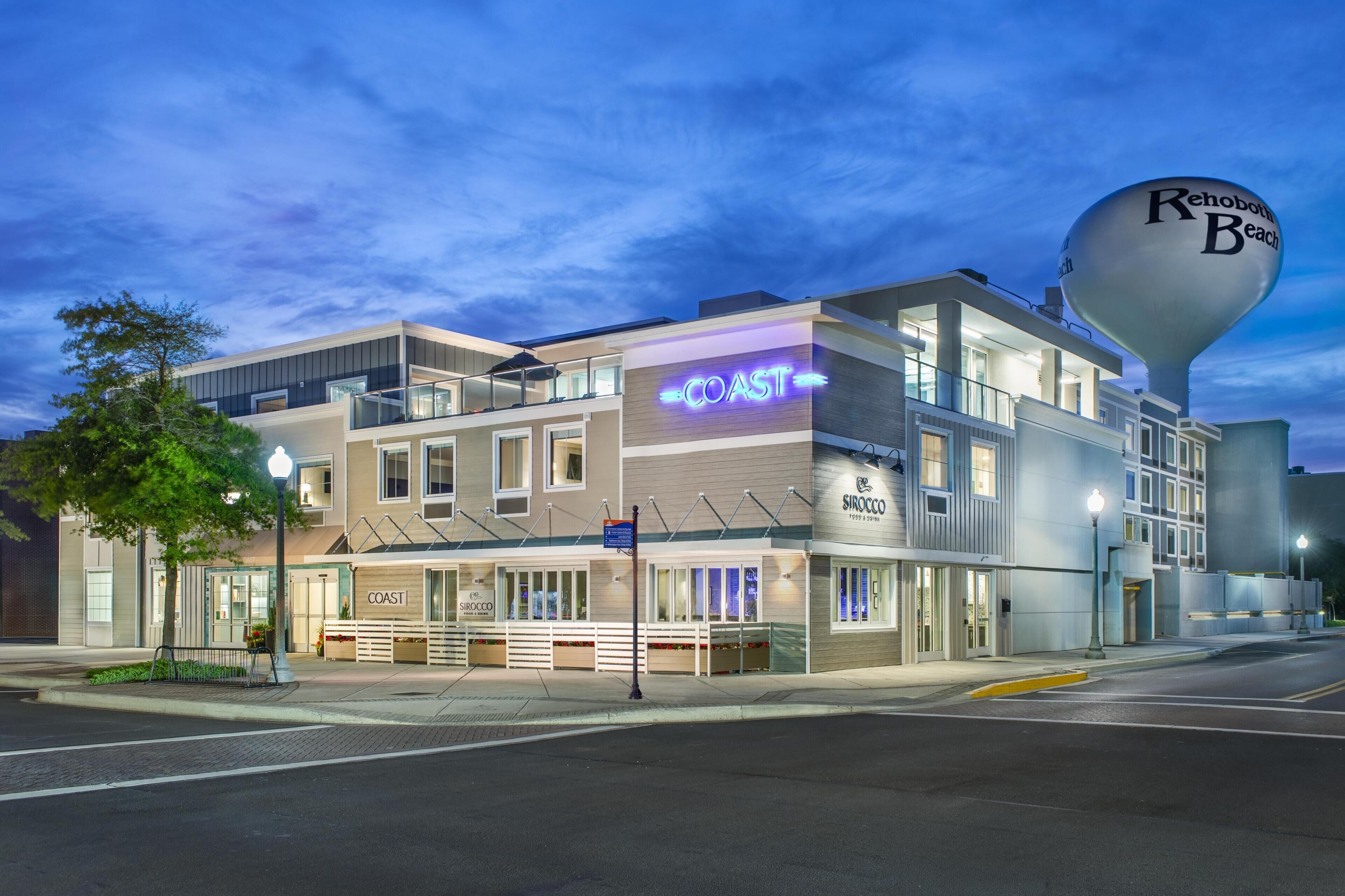 A multi-story hotel with a prominent 'COAST' sign, a water tower labeled 'Rehoboth Beach,' and a 'SIROCCO' sign.