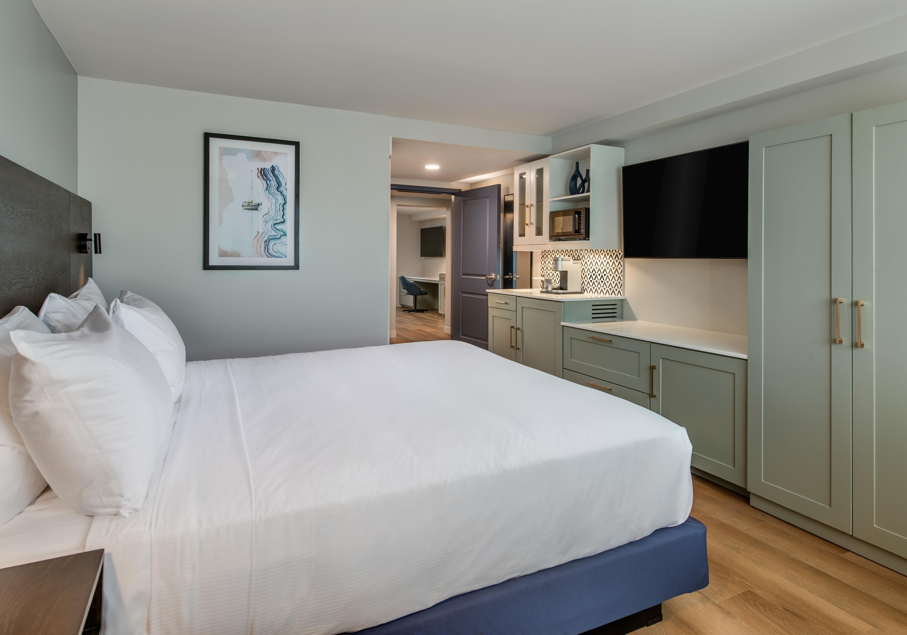 A modern hotel room with a large bed, a flat-screen TV, and a kitchenette.