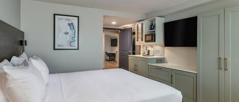 A modern hotel room with a large bed, a flat-screen TV, and a kitchenette.