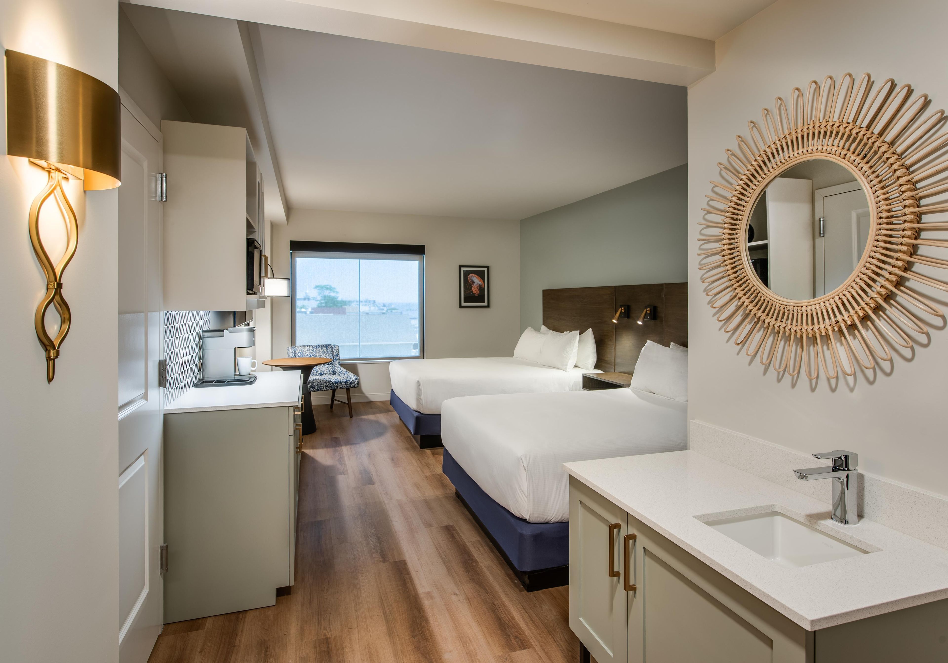 Habitación de hotel con kitchenette, dos camas, un espejo grande y vista al mar.