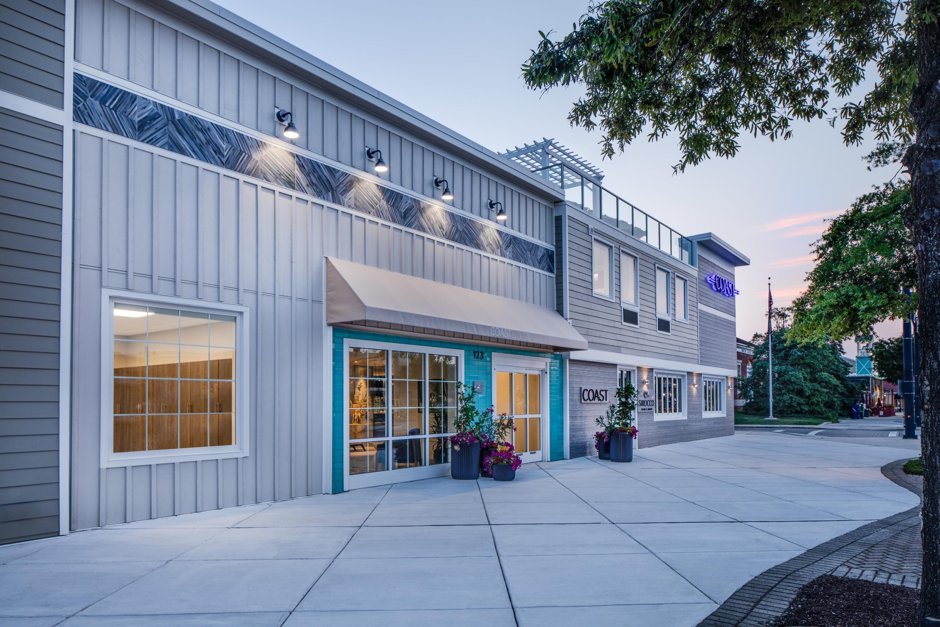 A modern building with a storefront, large windows, and outdoor seating area with potted plants.