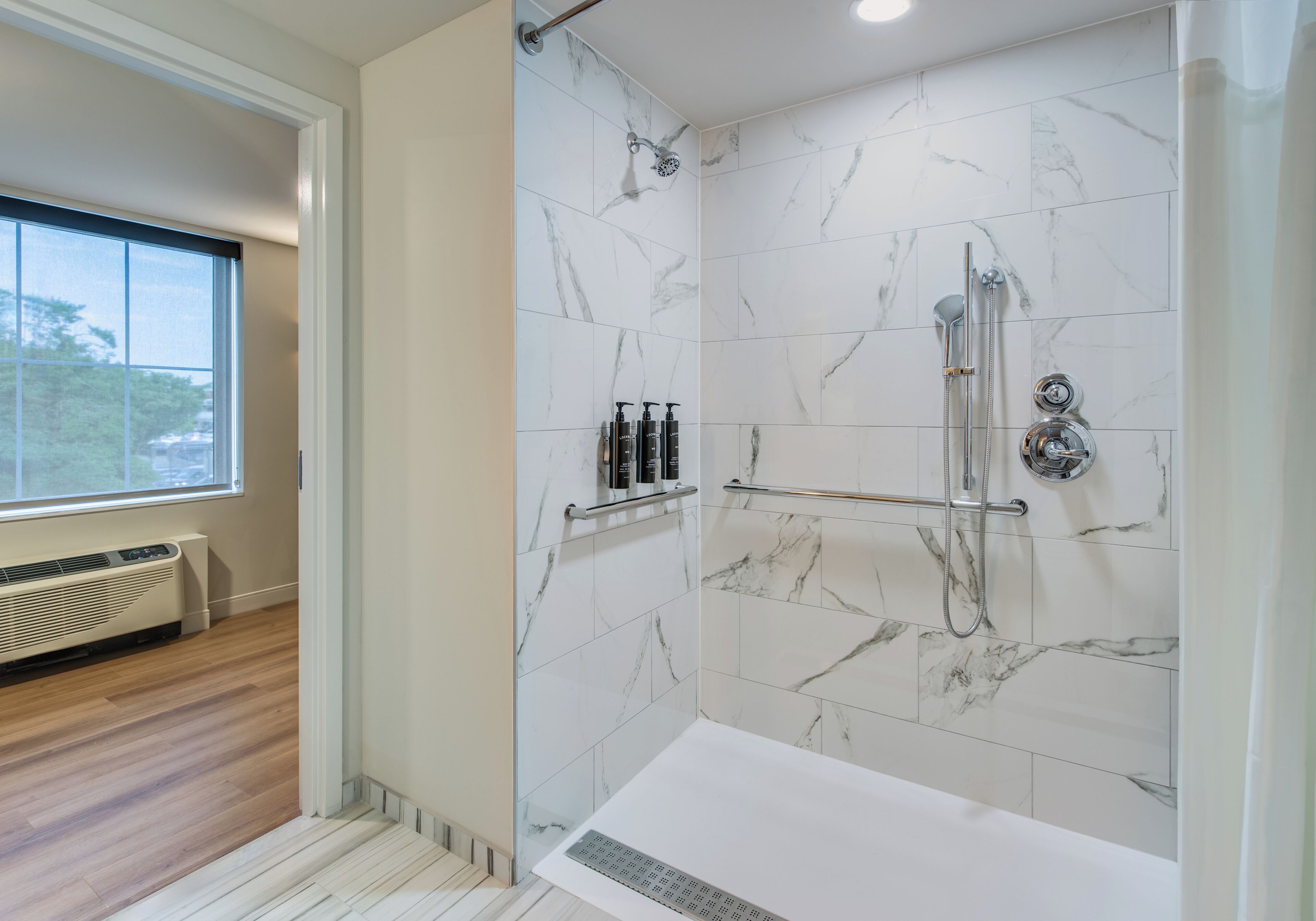 Un baño moderno con ducha a nivel, baldosas de mármol, ventana y calefacción integrada.
