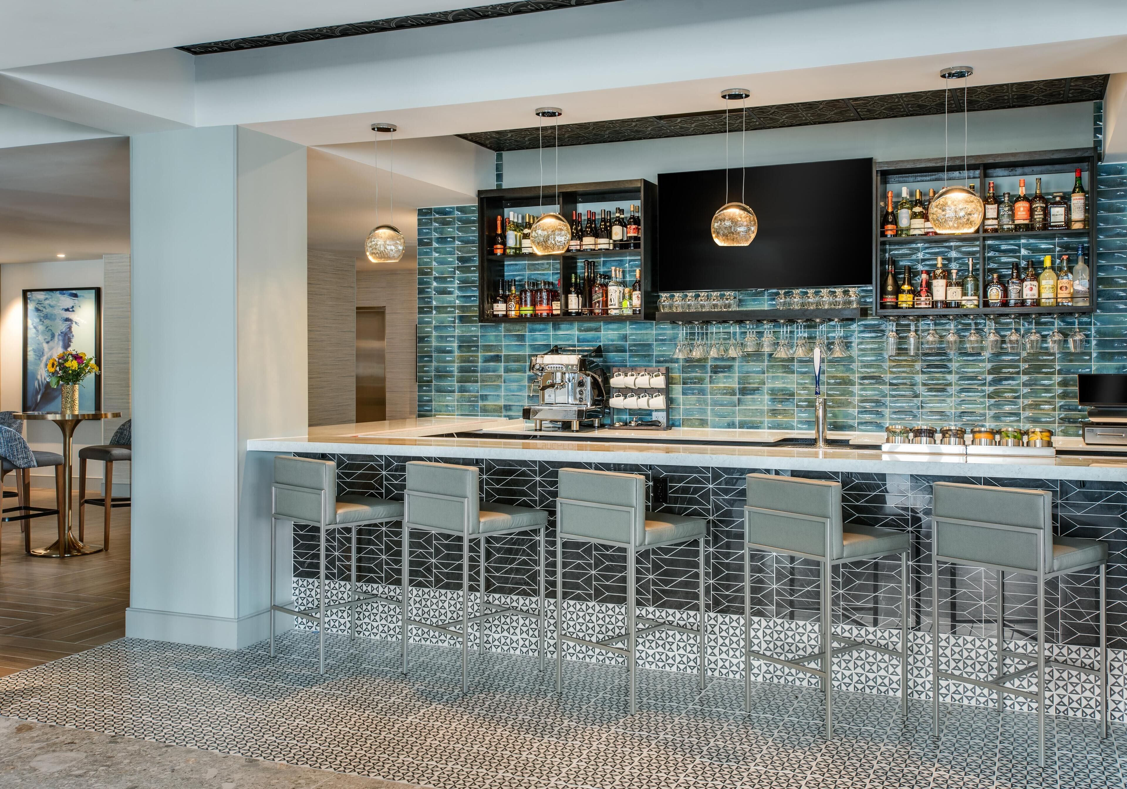 Zona de bar moderna con salpicadero de azulejos, taburetes y una variedad de botellas de licor.
