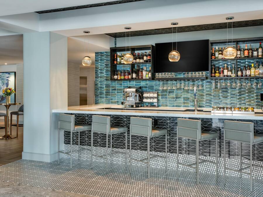 Zona de bar moderna con salpicadero de azulejos, taburetes y una variedad de botellas de licor.