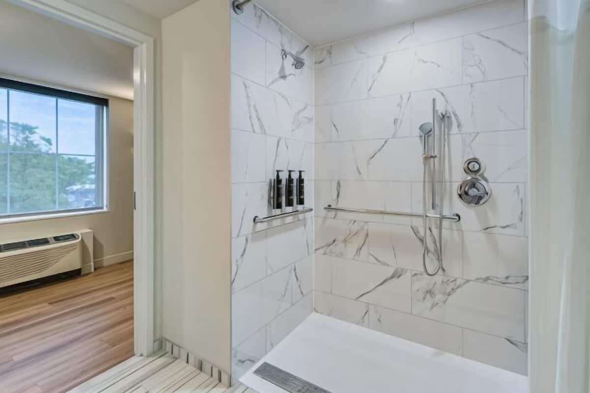 A bathroom with a shower, marble walls, a window, and a radiator.