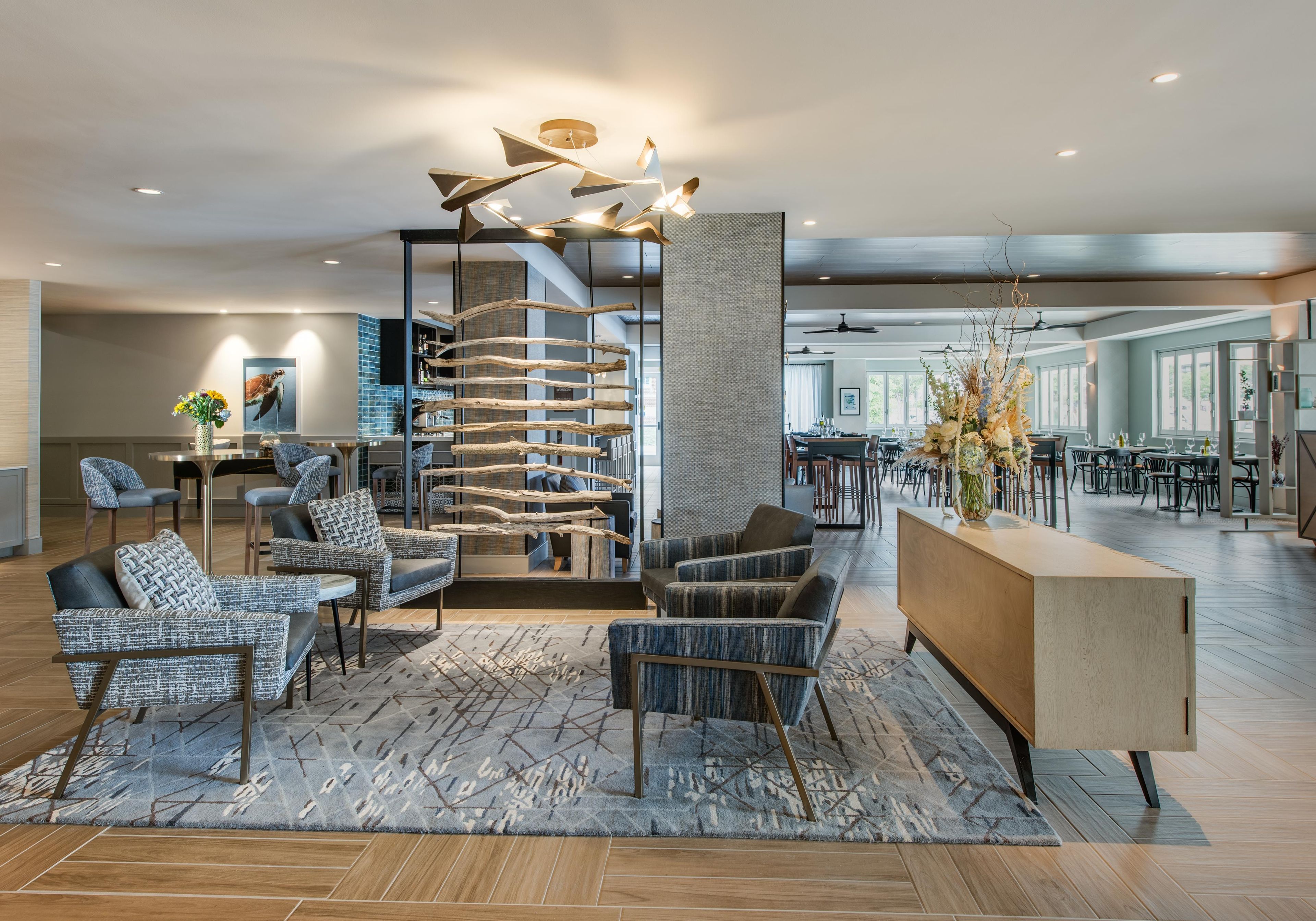 Un hall d’hôtel moderne avec un espace salon central, un comptoir d’accueil et, au fond, un espace repas.