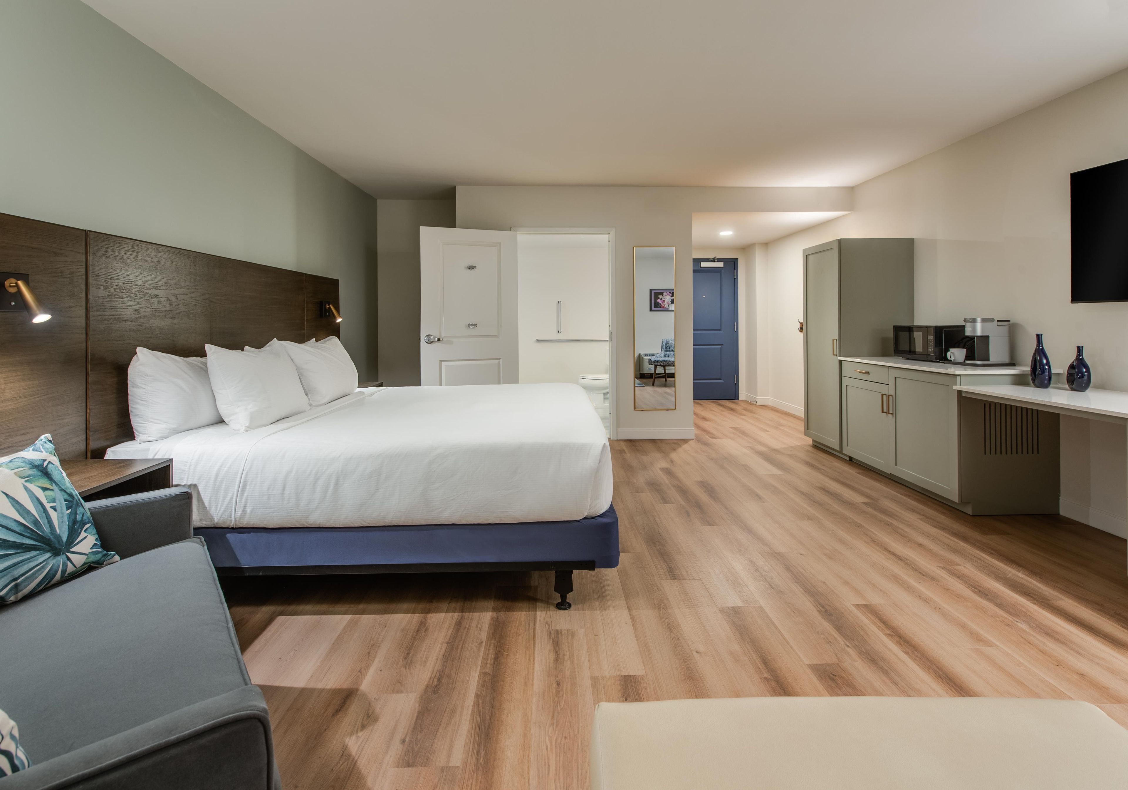 A modern hotel room with a large bed, a desk, and a kitchenette.