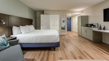 A modern hotel room with a large bed, a desk, and a kitchenette.