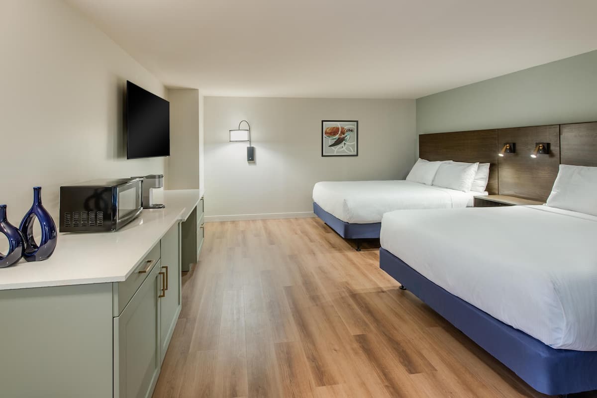 A hotel room with two beds, a flat-screen TV, a microwave, and a small kitchenette.