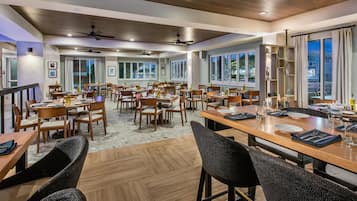 A spacious dining area with multiple tables and chairs, large windows, and ceiling fans.