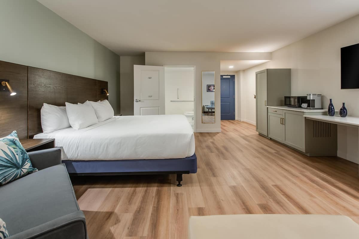A modern hotel room with a large bed, a desk, and a kitchenette.