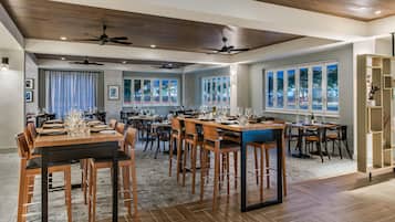 A spacious dining area with multiple tables and chairs, ceiling fans, and large windows.