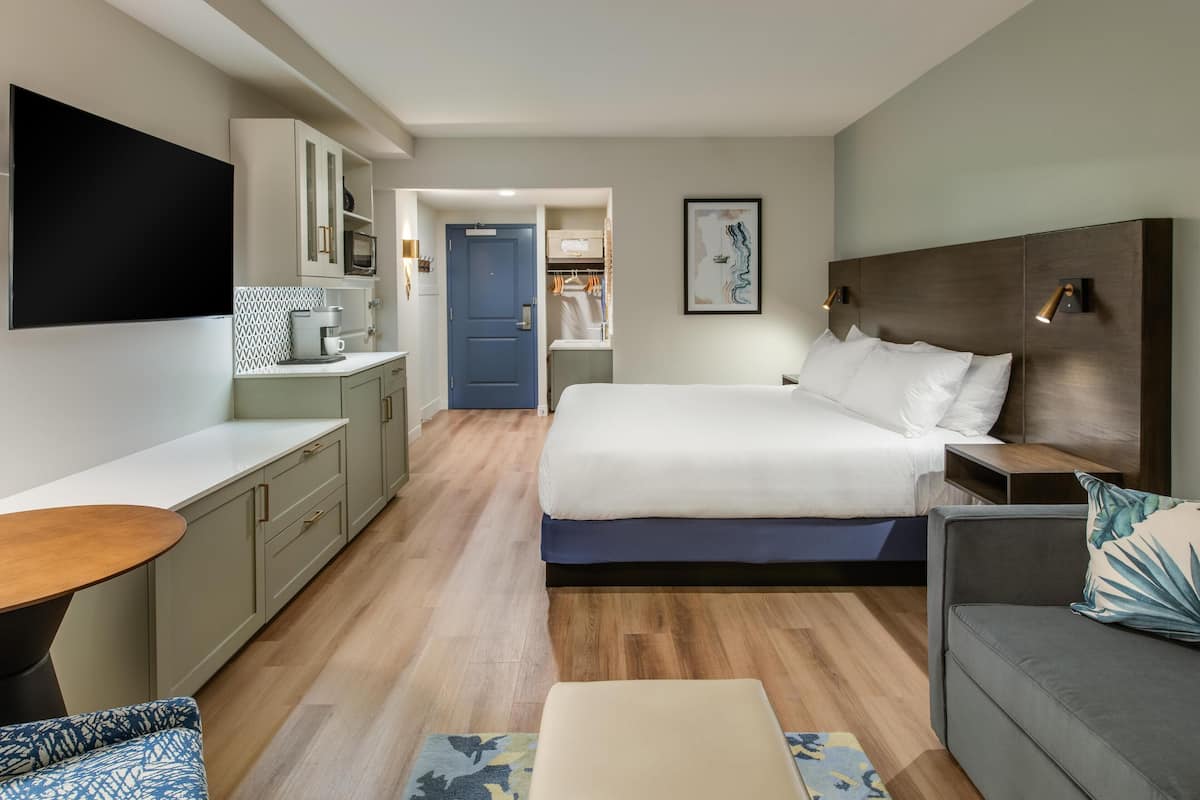 A modern hotel room with a large bed, a desk, a sofa, and a TV mounted on the wall.