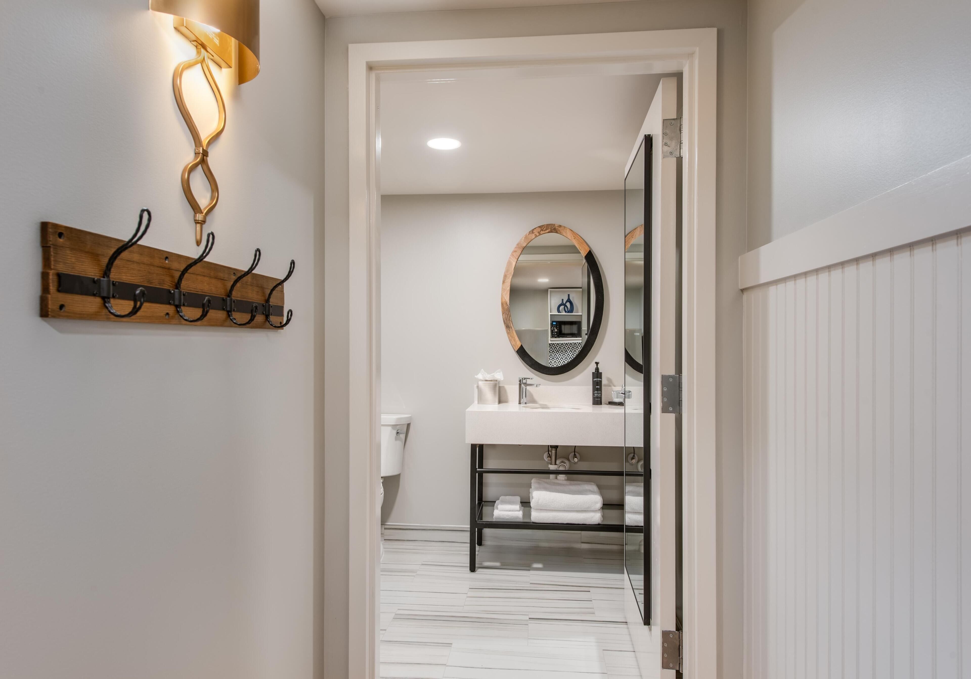 A hallway leading to a bathroom with a white toilet, a towel rack, and a mirror.