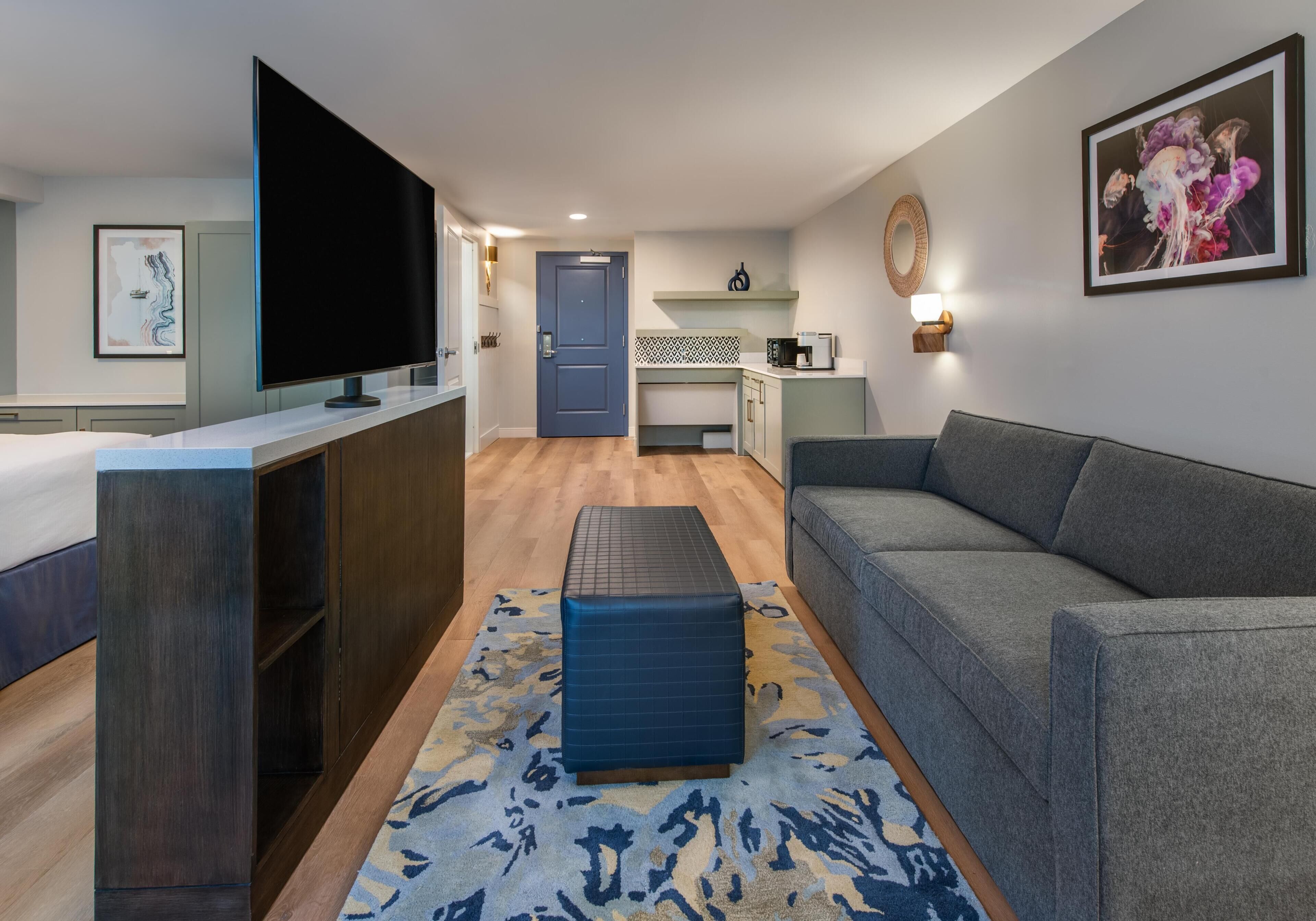 A modern living room with a sofa, a TV, a coffee machine, and a kitchen area in the background.