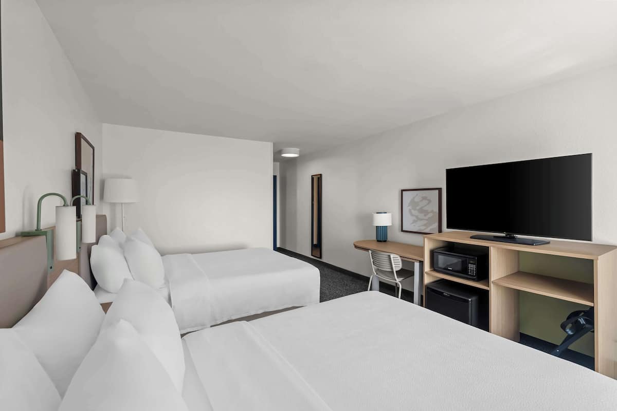 A hotel room with two beds, a desk with a television, a microwave, and a chair.