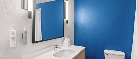 Un baño con un lavamanos blanco, un espejo y un inodoro frente a una pared azul.