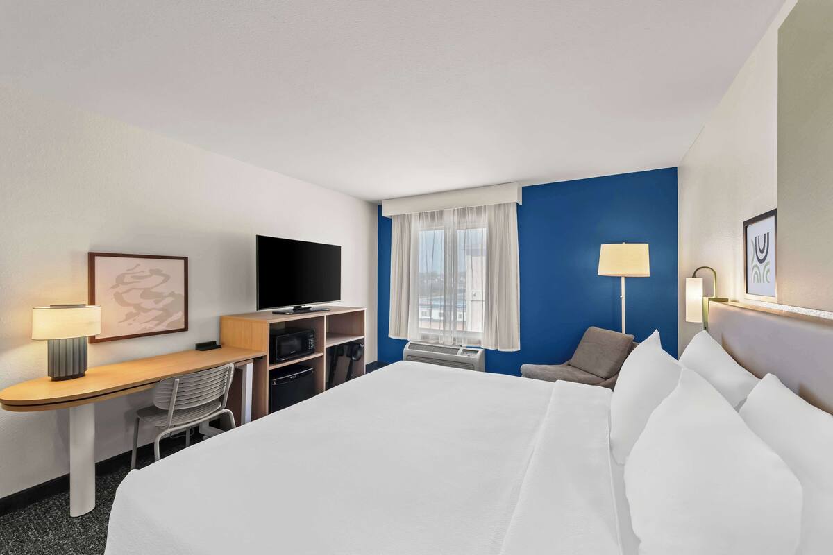 A hotel room with a bed, desk, chair, TV, and window.