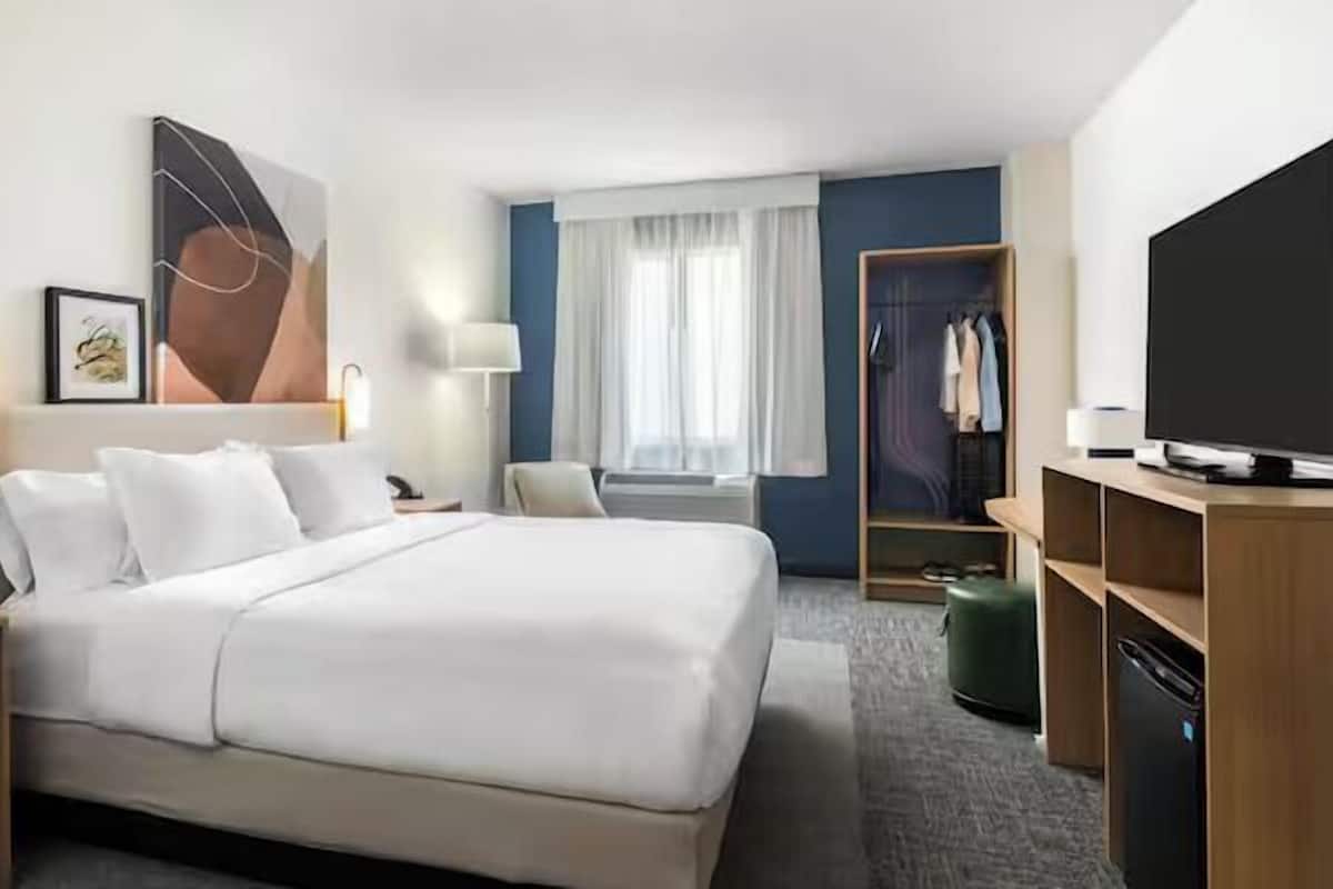 A hotel room with a large bed, a desk, a wardrobe, and a television.