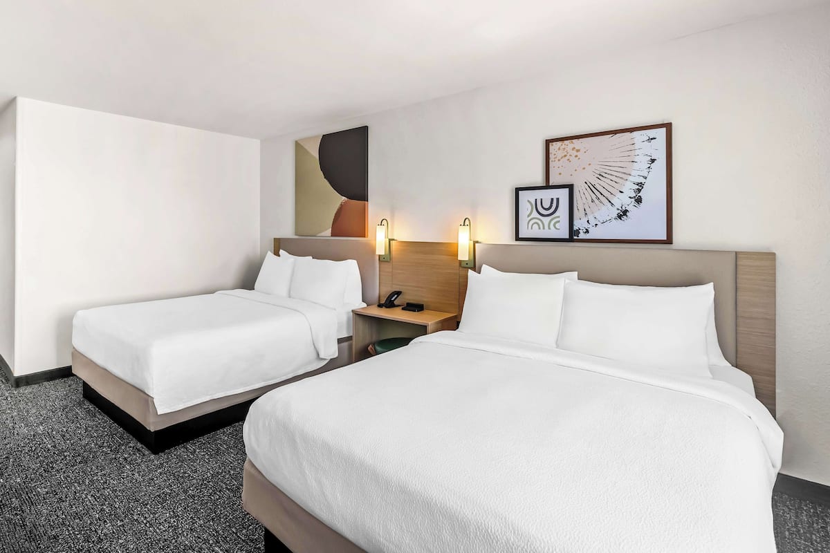 A hotel room with two beds, a nightstand with a phone, and wall art.