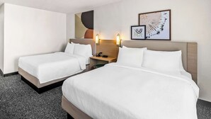 Una habitación de hotel con dos camas, una mesita de noche con teléfono y una obra de arte en la pared.