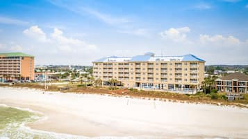 Un hotel frente al mar con varios pisos, una zona de piscina y una playa en primer plano.