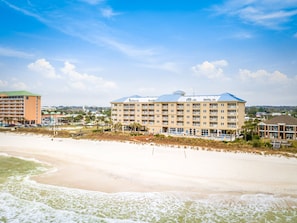 A beachfront hotel with multiple floors, a pool area, and a beach in the foreground.