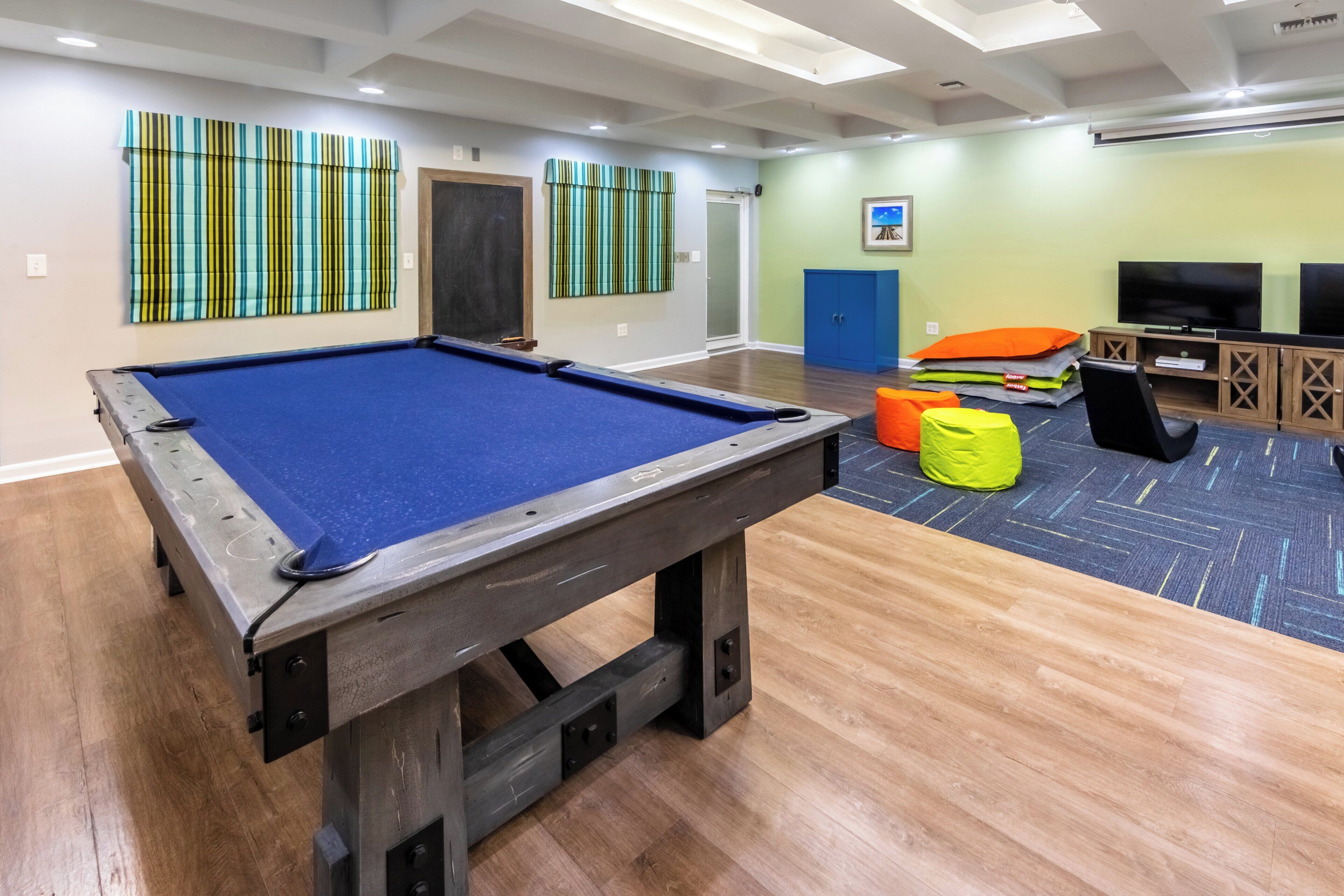 Una mesa de billar en una habitación con suelo de madera, pared azul y una puerta.