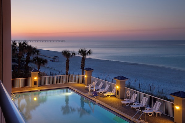 A poolside area with lounge chairs and a view of the ocean at dusk.