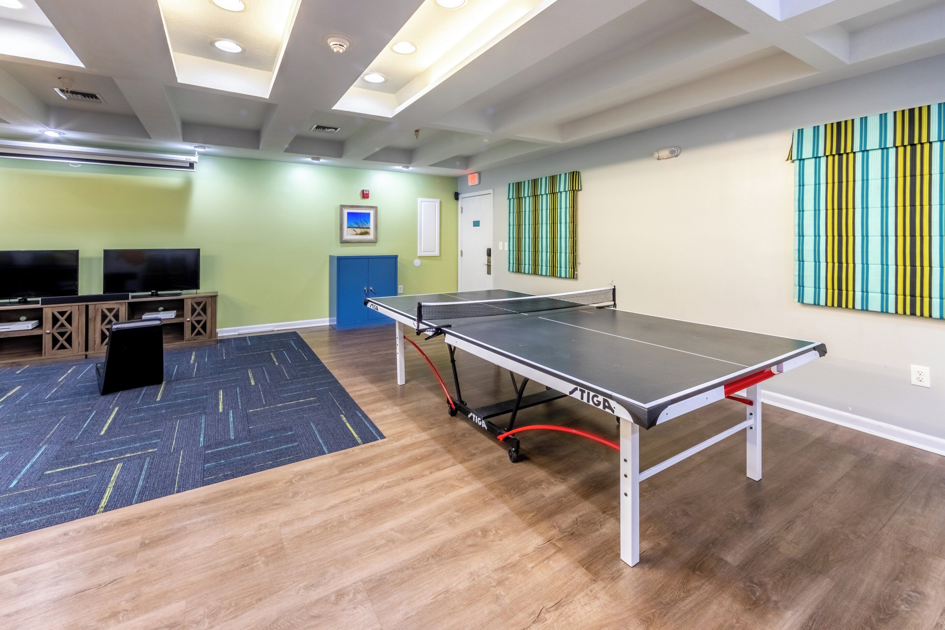 A room with a ping pong table, a television, and a blue cabinet.