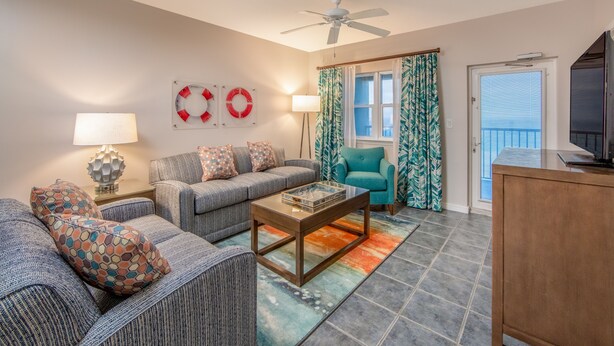A living room with a sofa set, a coffee table, a teal armchair, and a television.