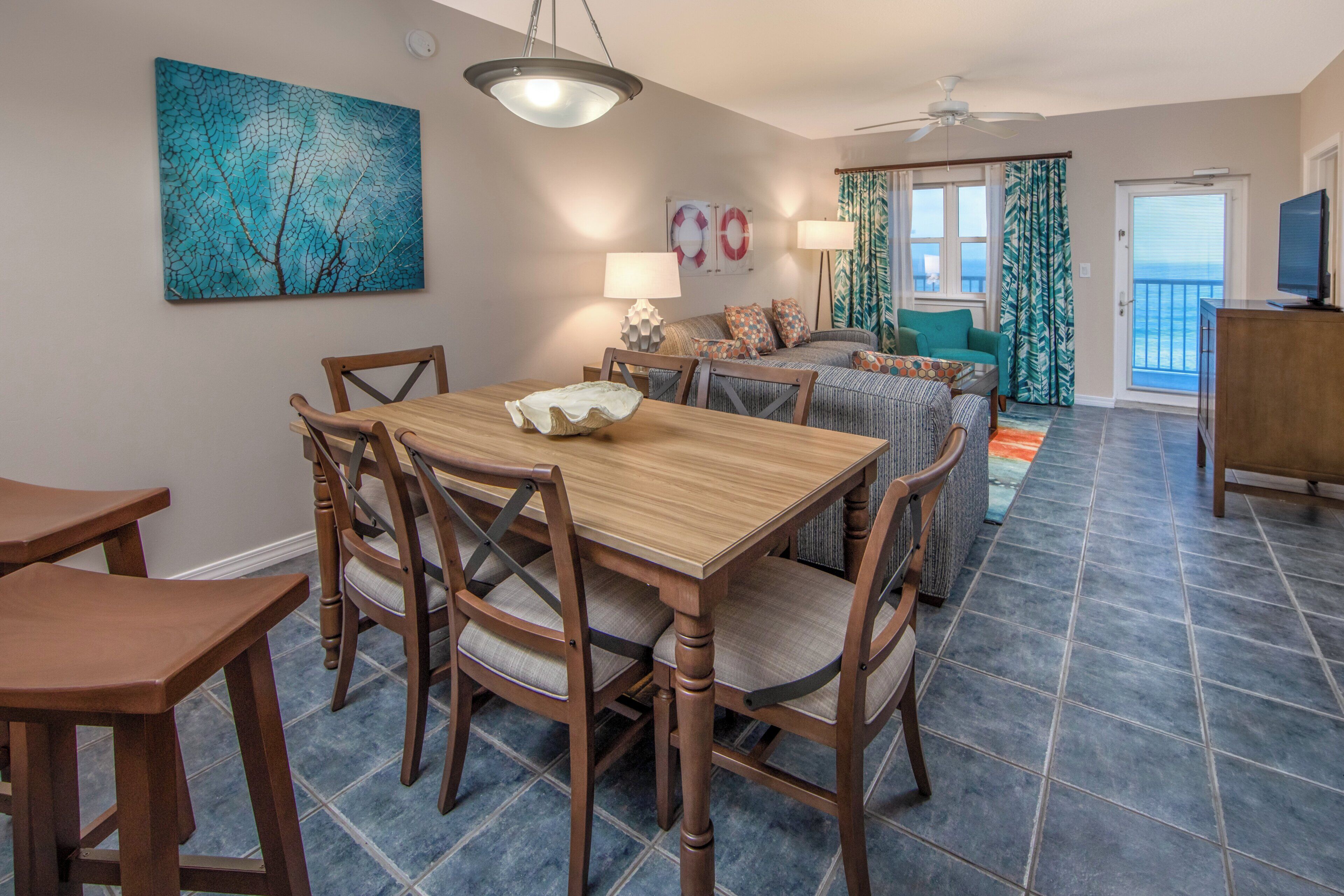 Un coin repas avec une table et des chaises en bois, un ventilateur de plafond et une vue sur l’extérieur par une fenêtre.