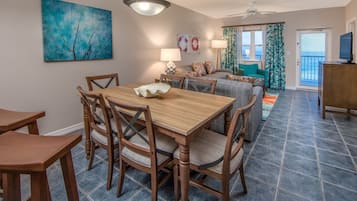 Un comedor con una mesa y sillas de madera, un ventilador de techo y vistas al océano a través de un ventanal corredera.