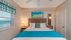A bedroom with a bed, a ceiling fan, a nightstand with a lamp, a window with blinds, and a door.