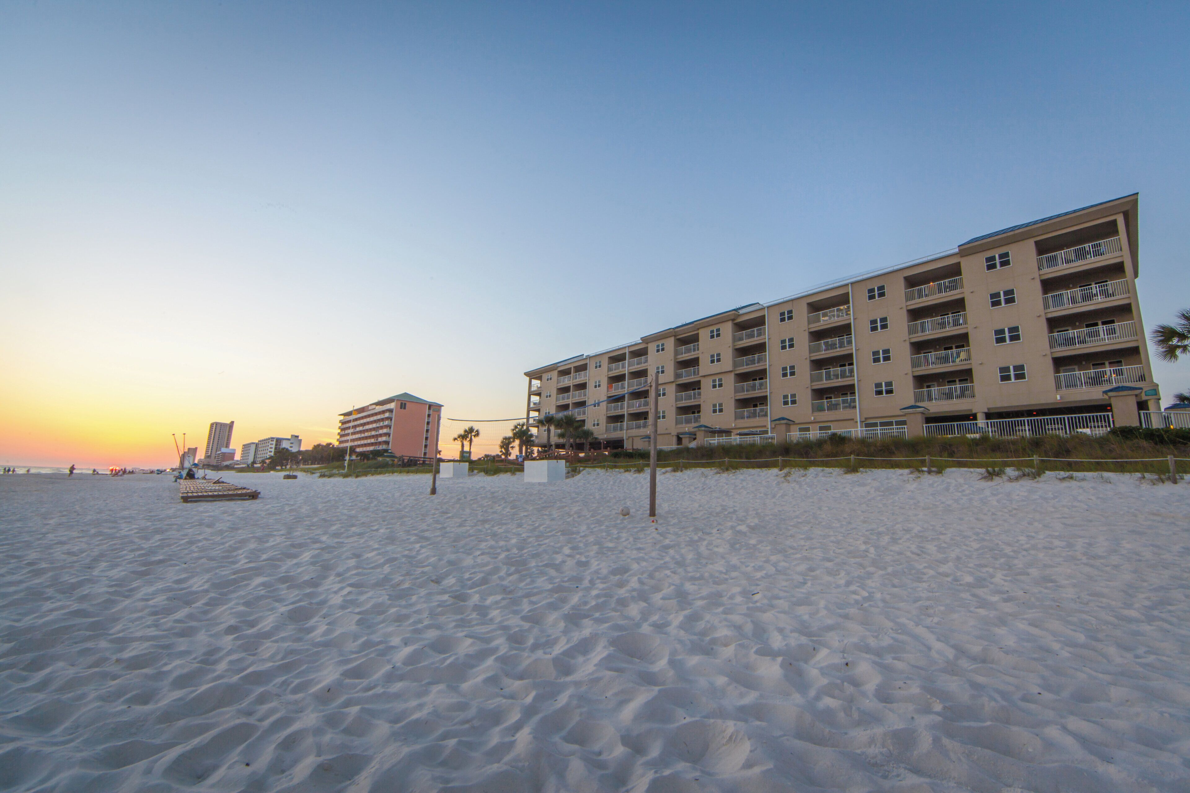 Un hôtel en bord de mer, avec plusieurs étages, des balcons et une plage de sable au premier plan.
