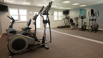 A fitness center with various exercise machines, including treadmills and stationary bikes, arranged in a spacious room with carpeted flooring and large windows.