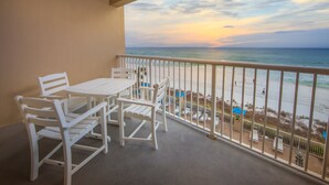 A balcony with a table and chairs, overlooking a beach with people and umbrellas.