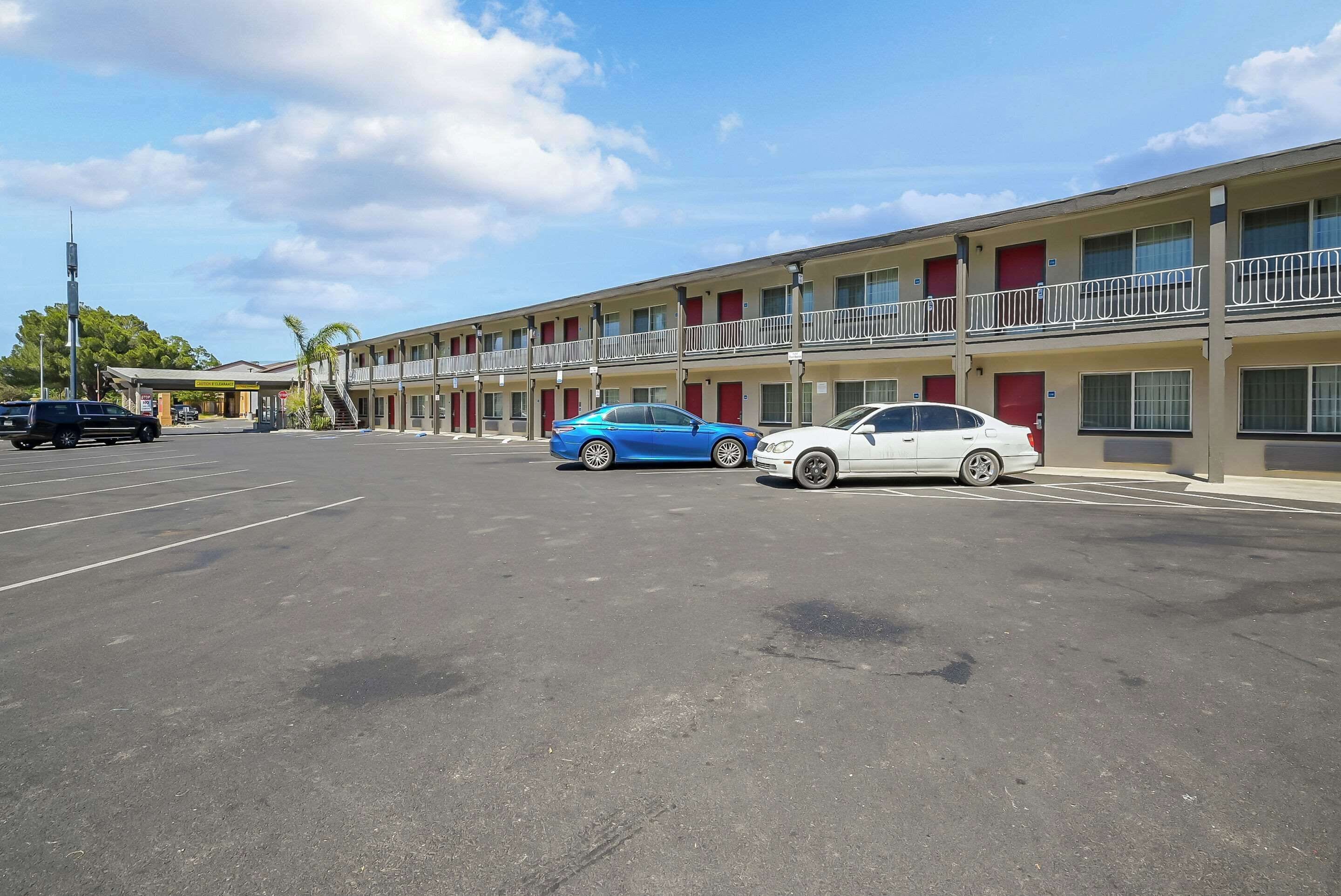 A motel with a parking lot, two cars parked in front, and a clear sky.