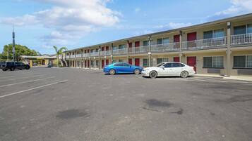 A motel with a parking lot, two cars parked in front, and a clear sky.
