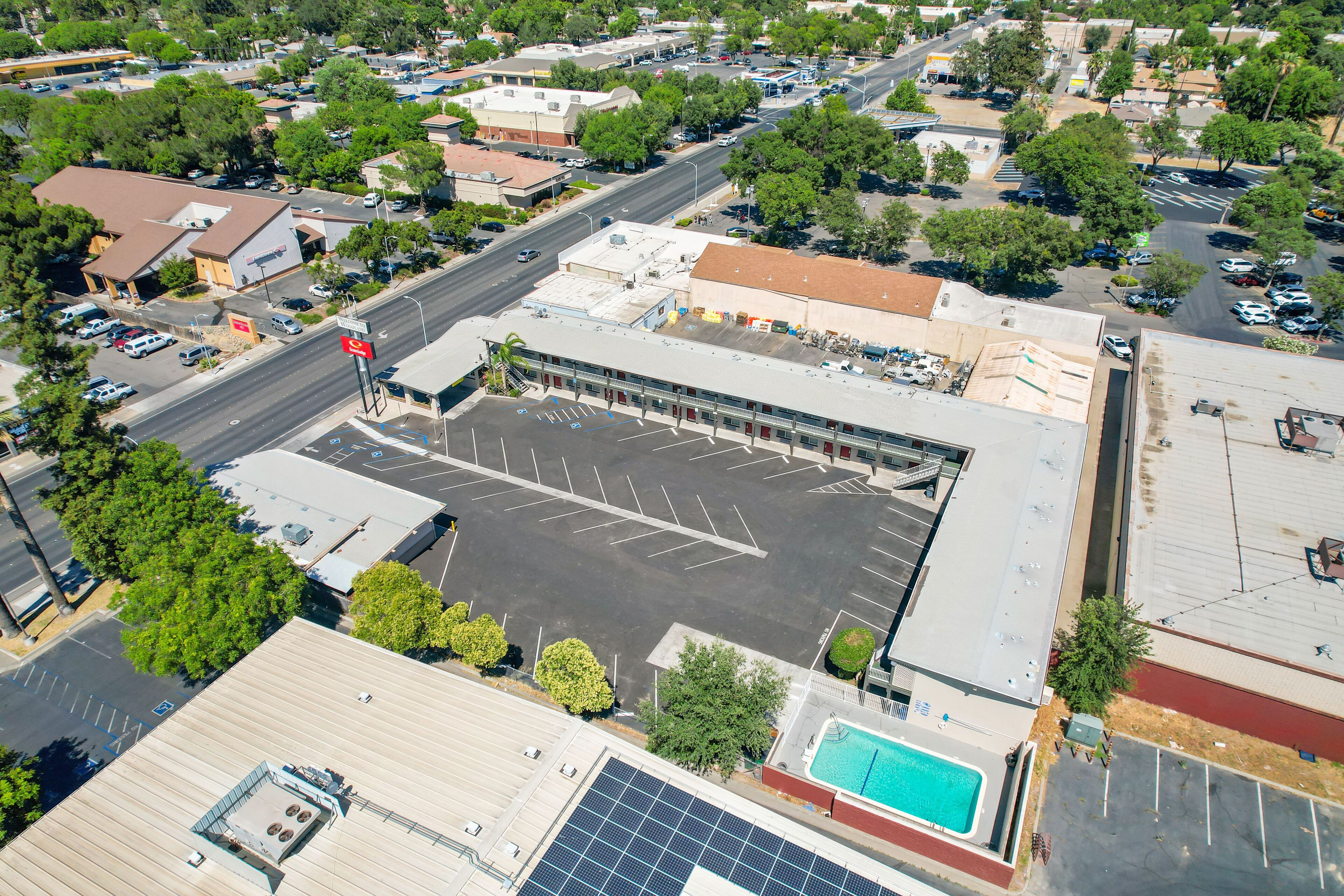 An aerial view of a commercial building with a parking lot, solar panels, and a swimming pool.