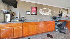 Una cocina con armarios de madera, encimera de granito, cafetera, ordenador y televisor montado en la pared.